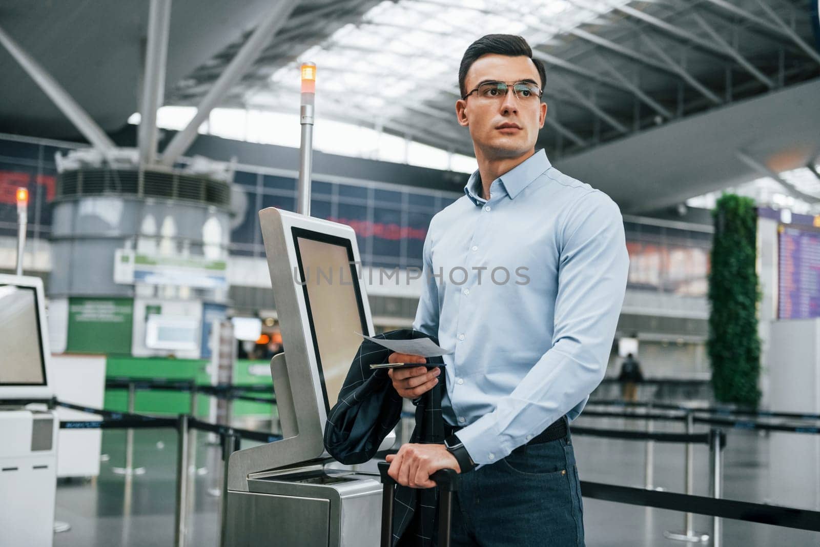 Standing by the terminal. Young businessman in formal clothes is in the airport at daytime.