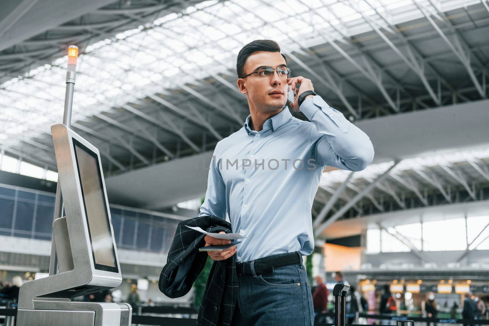 Holding phone. Young businessman in formal clothes is in the airport at daytime.