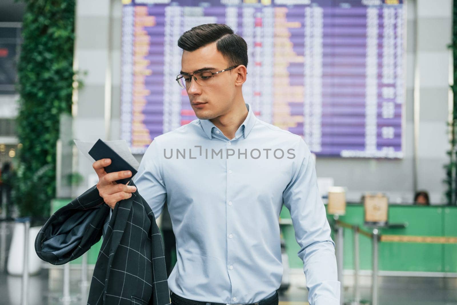 Holding phone. Young businessman in formal clothes is in the airport at daytime.