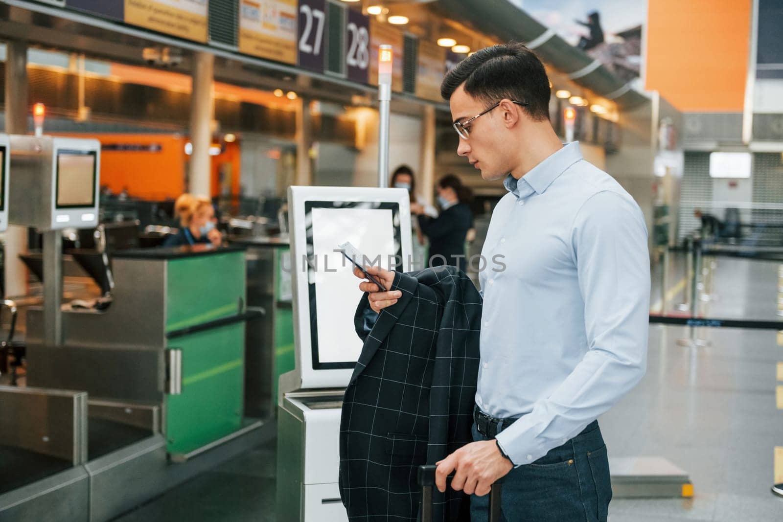 Holding phone. Young businessman in formal clothes is in the airport at daytime.