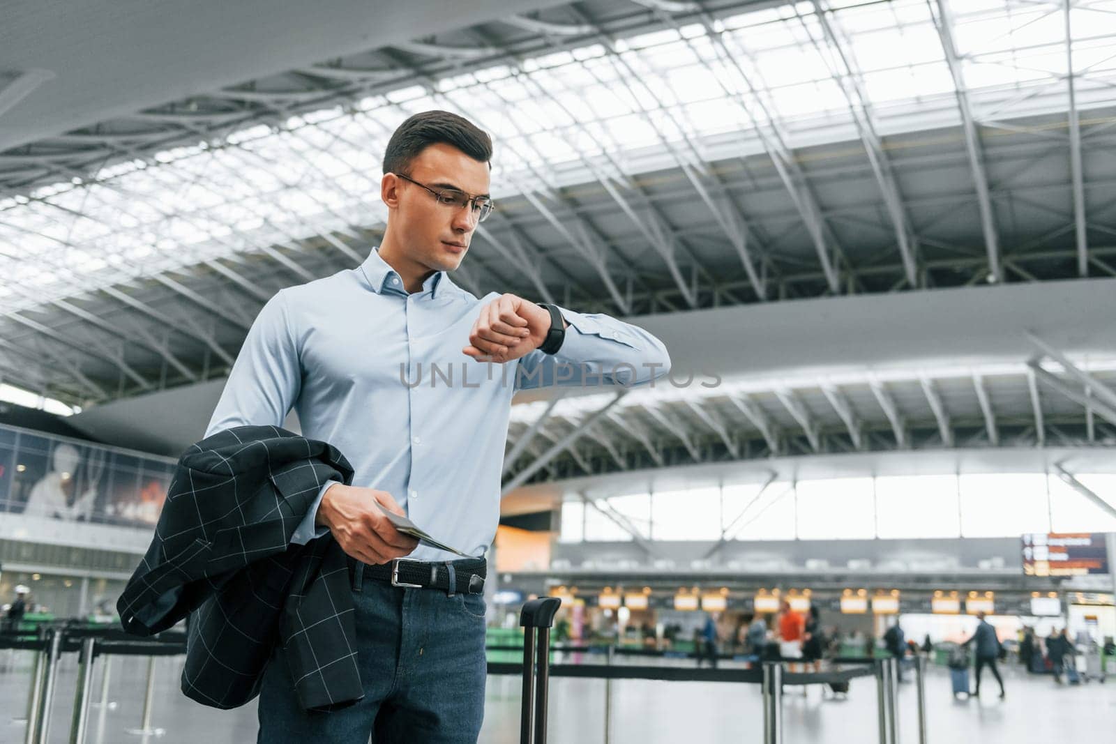 Checking the time. Young businessman in formal clothes is in the airport at daytime by Standret