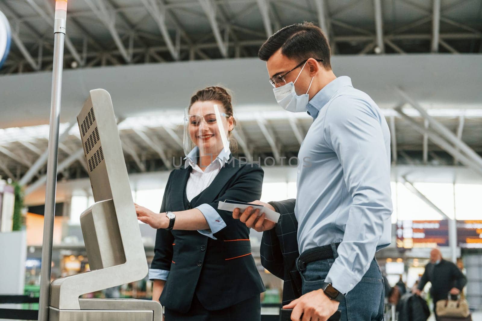 Employee helping using terminal. Young businessman in formal clothes is in the airport at daytime.