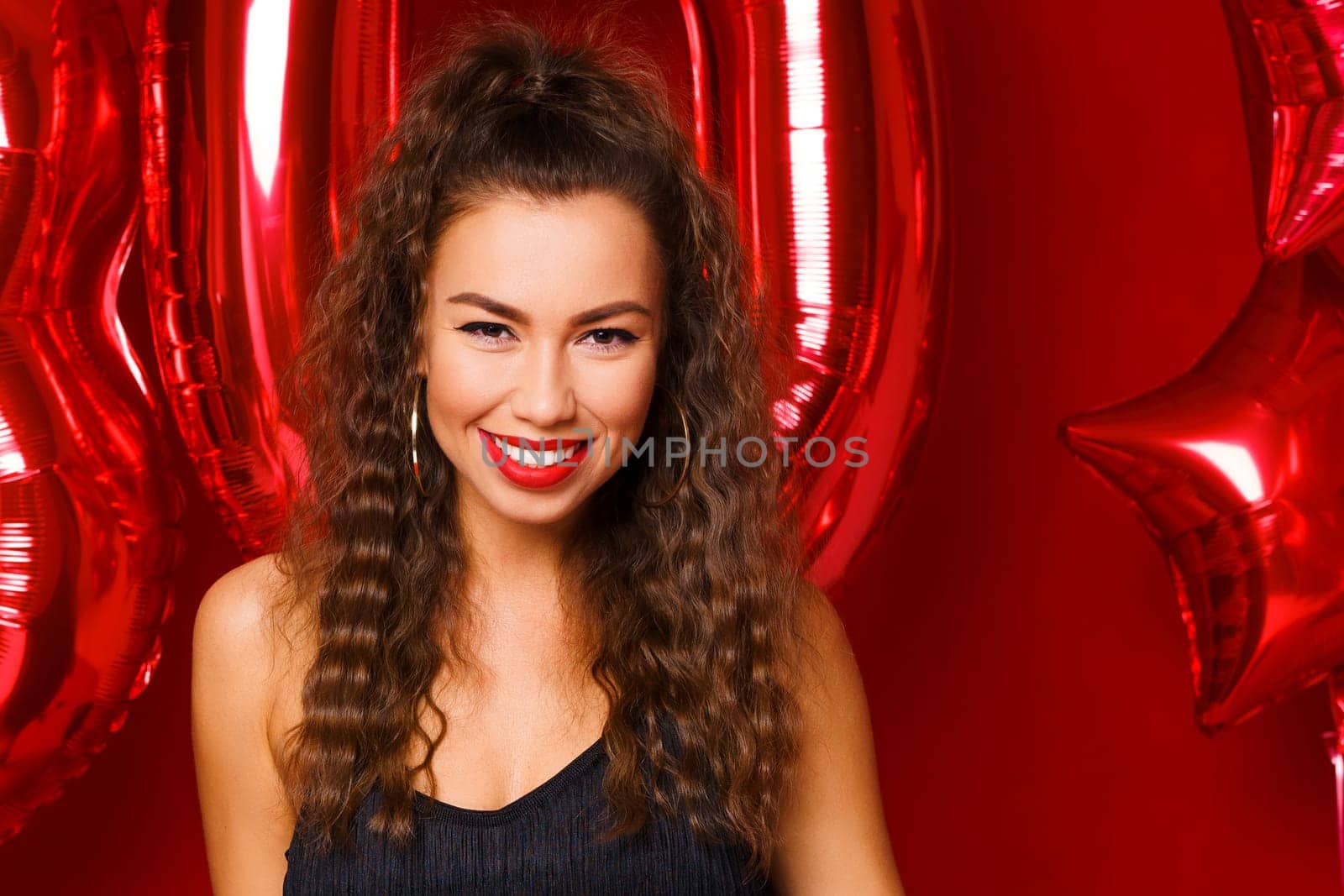 Portrait of happy 30 year old woman on red background with red balloons. A beautiful girl of Caucasian appearance is celebrating her anniversary. Balloons in the form of numbers 30 and stars.