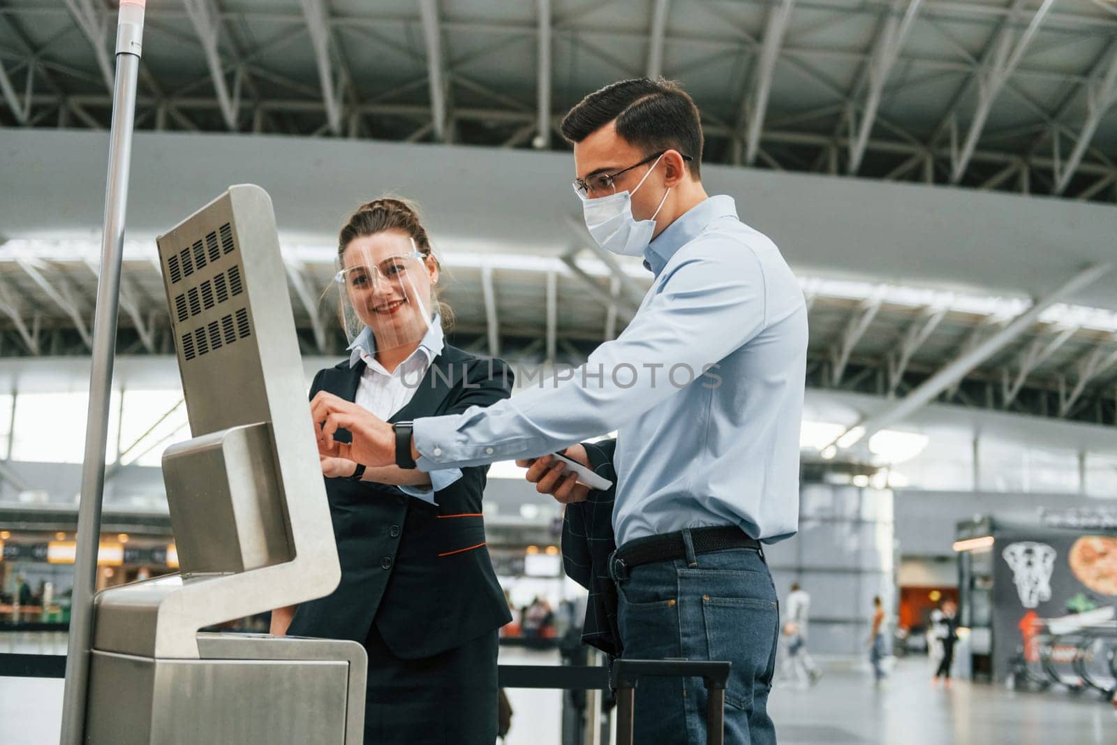 Employee helping using terminal. Young businessman in formal clothes is in the airport at daytime by Standret