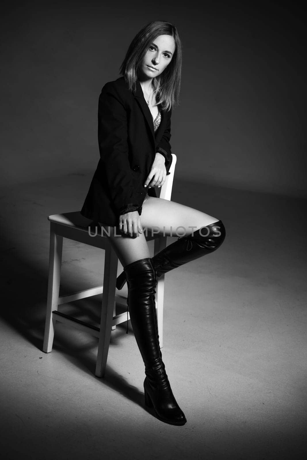 beautiful woman of Caucasian ethnicity posing sitting on a chair in a black jacket and lingerie, black and white photo. Dark photo of seductive sexy girl
