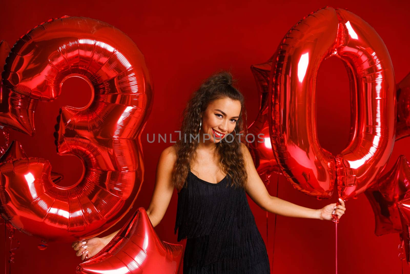Valentine Beauty girl with red balloon. Beautiful Happy Caucasian Young woman Holiday party, birthday. Joyful model - Image. On a red background, red balloons in the form of numbers 30
