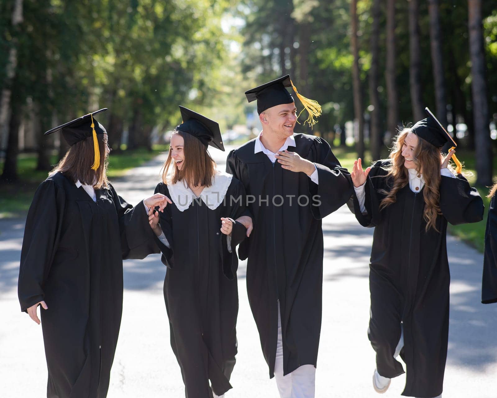 Row of happy young people in graduation gowns outdoors. Students are walking in the park