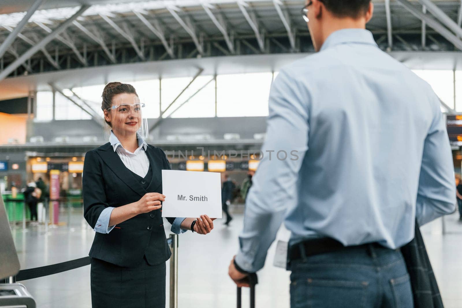 Meet by the woman with text. Young businessman in formal clothes is in the airport at daytime.