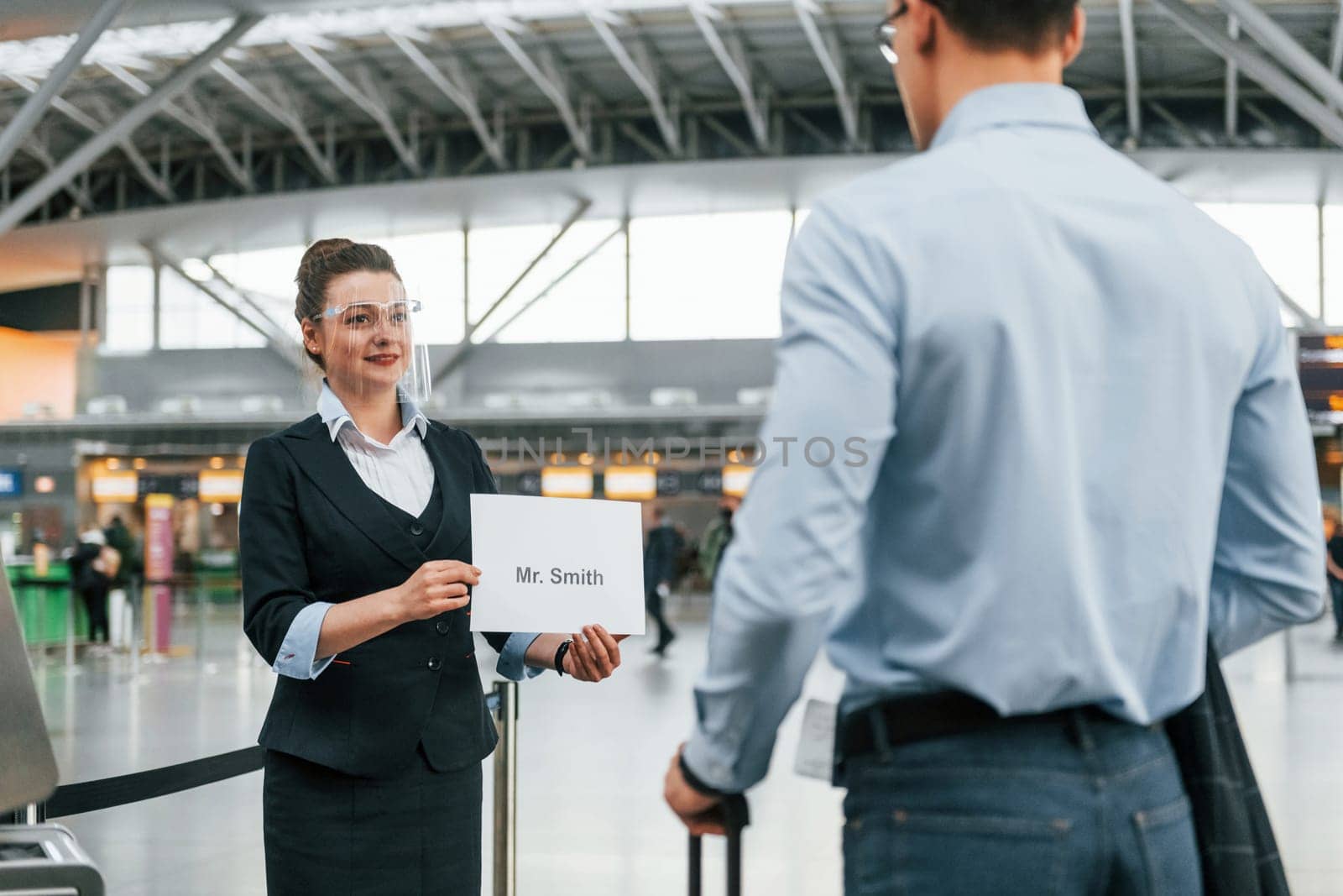 Meet by the woman with text. Young businessman in formal clothes is in the airport at daytime by Standret