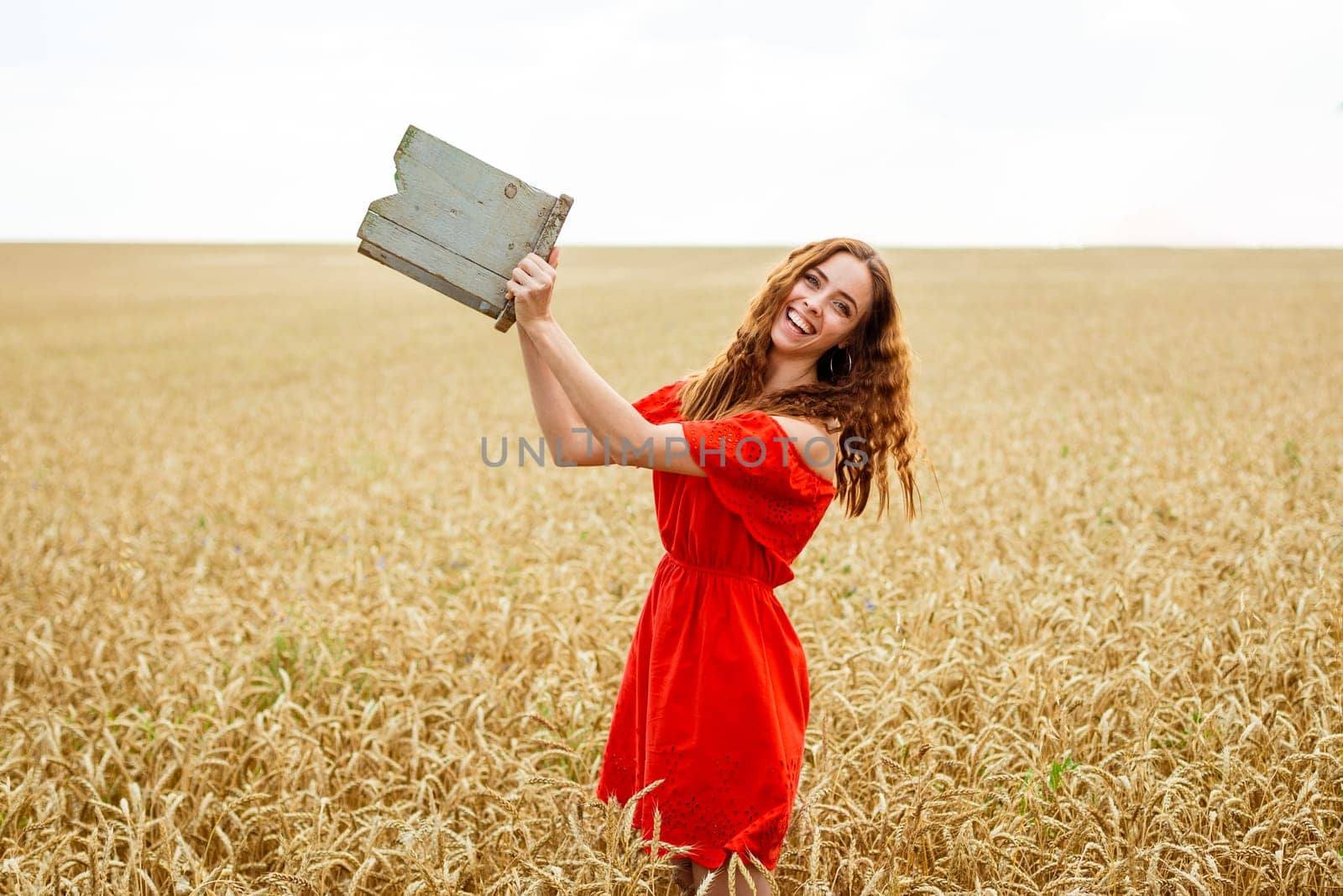 Style redhead young woman in red dress tay view yellow wheat field Happy girl with curly hair in field. Sweet smile on face of lovely free girl. Caucasian real girl. Happy woman enjoying freedom.