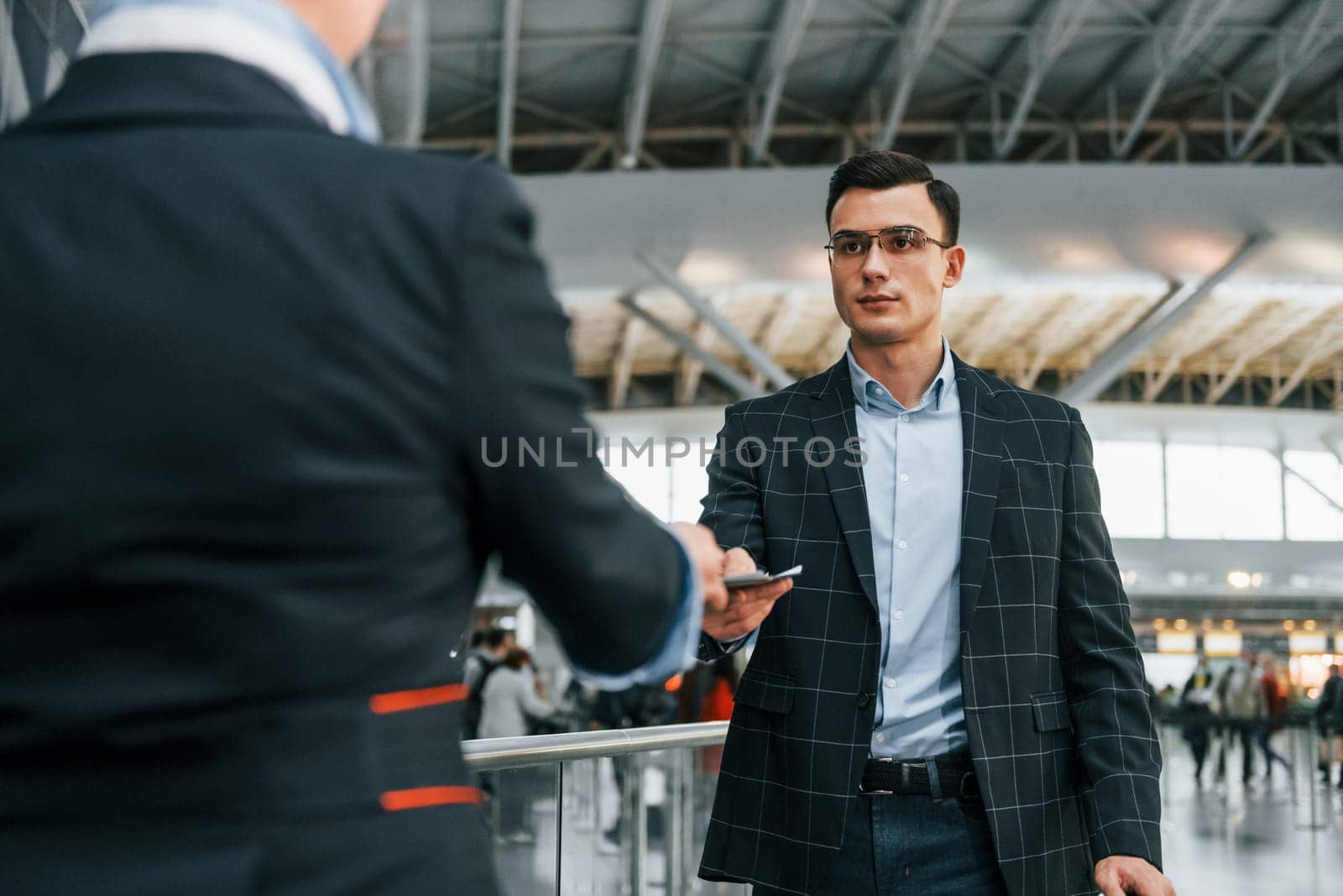 Giving the documents. Young businessman in formal clothes is in the airport at daytime.