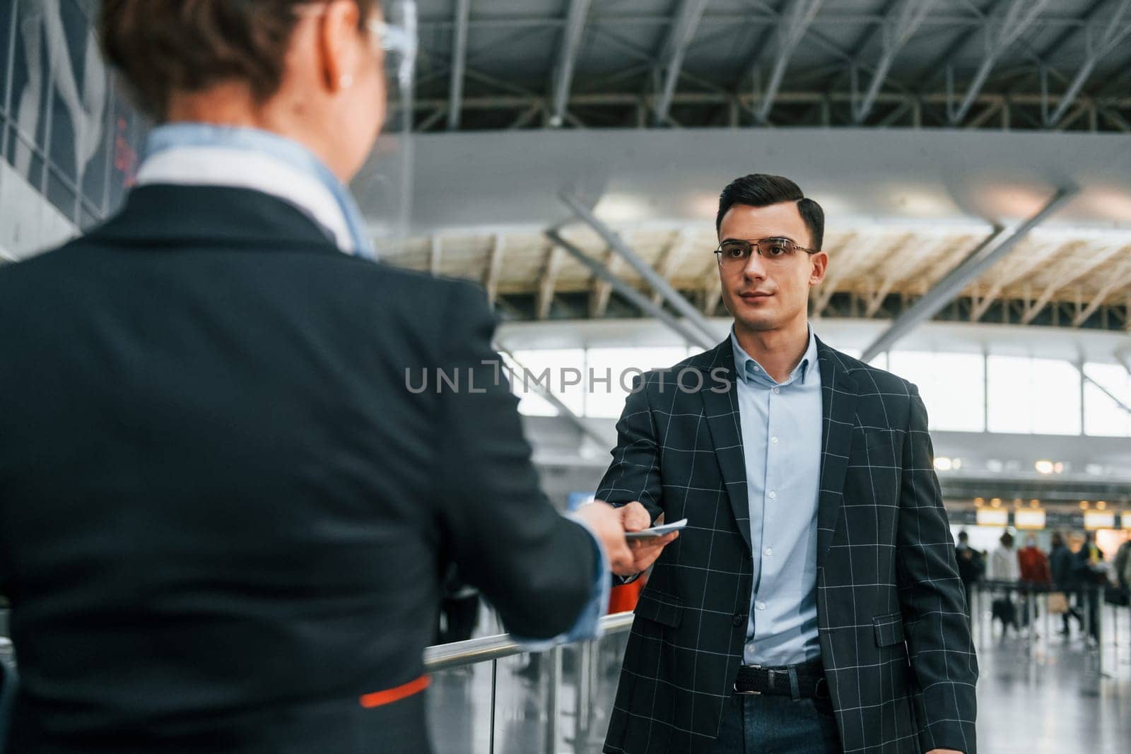 Giving the documents. Young businessman in formal clothes is in the airport at daytime.