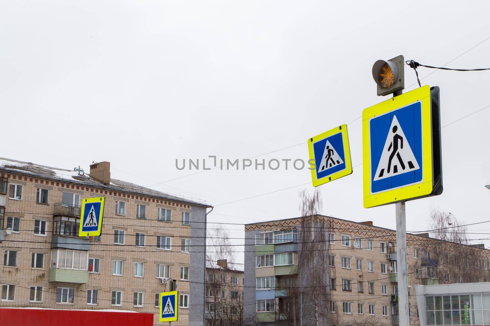 Road signs man in a blue square, means a pedestrian crossing. The yellow traffic light warning light is on. Close-up on the background of residential buildings. There is a copy space.