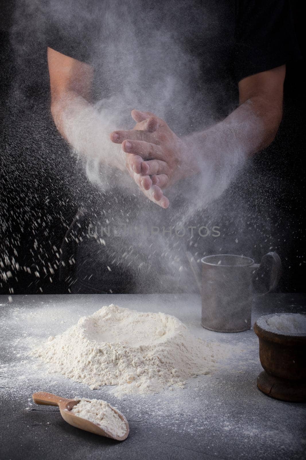 Baker clapping hands of flour on black background