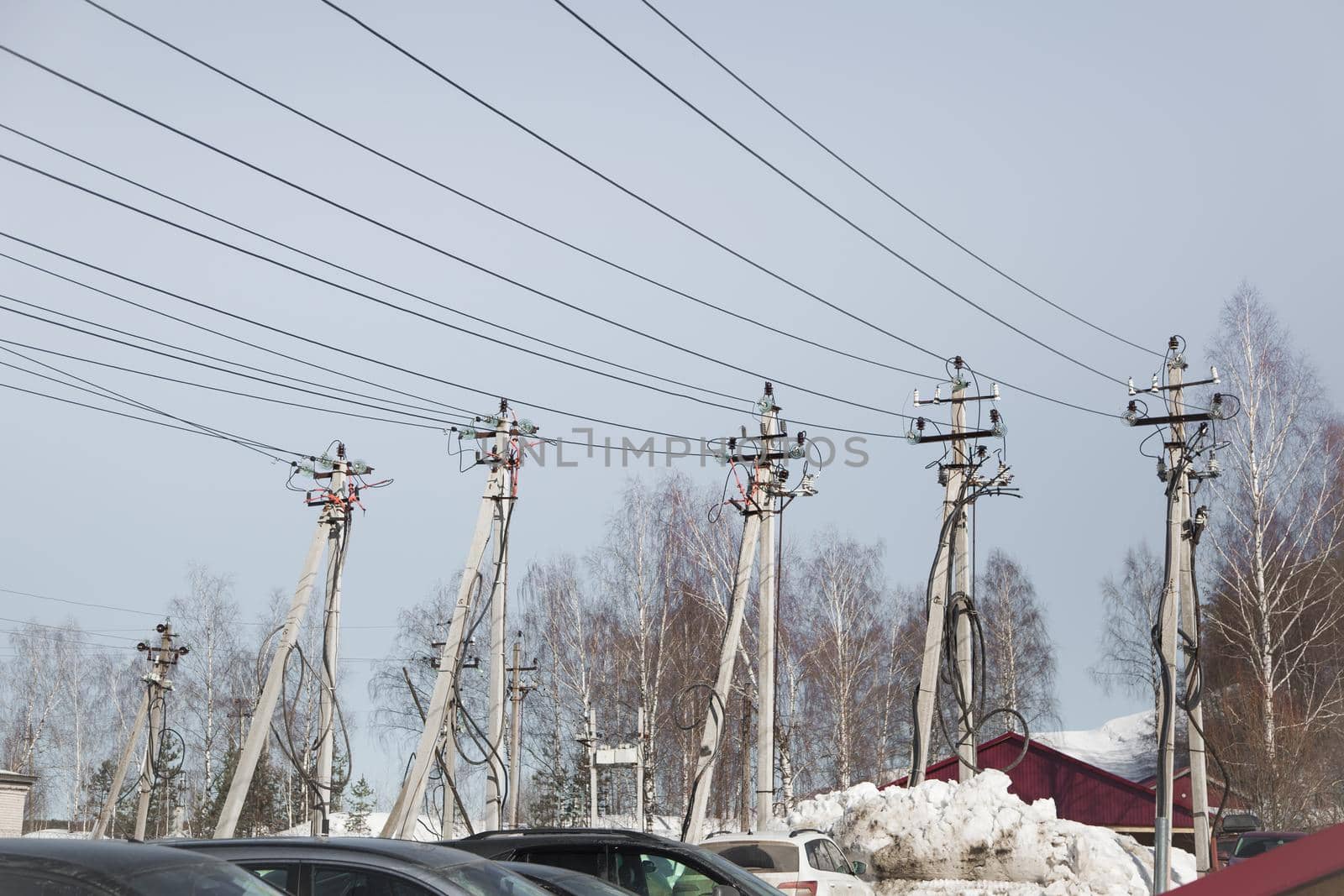 Electricity concept, concrete pillars with high voltage wires. Against the background of the blue sky, trees and snowdrifts. Power line close to high voltage transformer station.