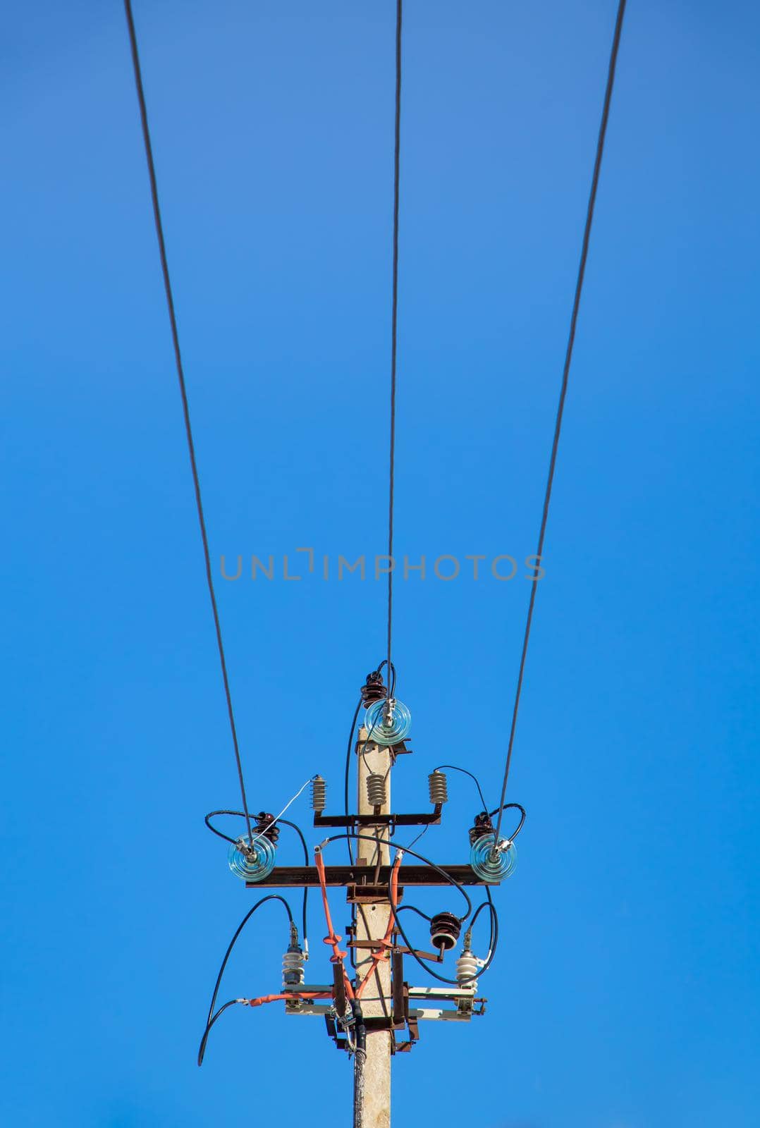 Electricity concept, top of a concrete pillar with high voltage wires. Close-up against the blue sky. Power line close to high voltage transformer station.
