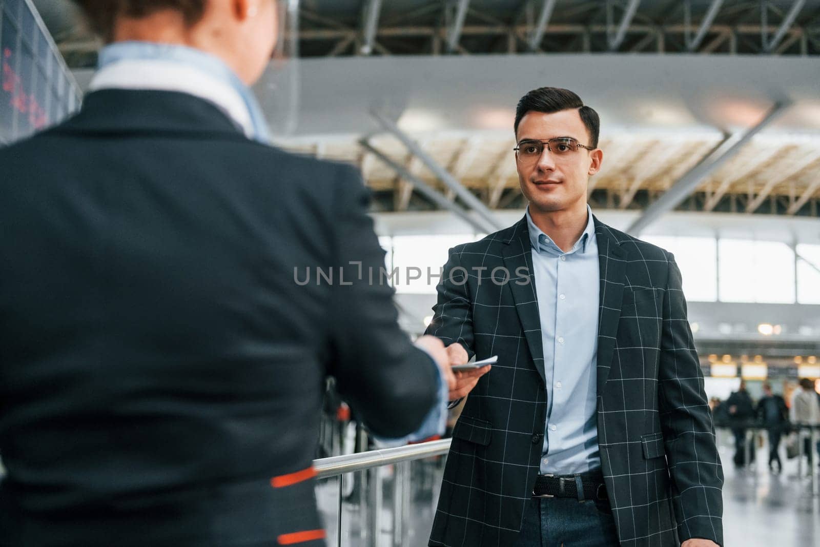 Giving the documents. Young businessman in formal clothes is in the airport at daytime.