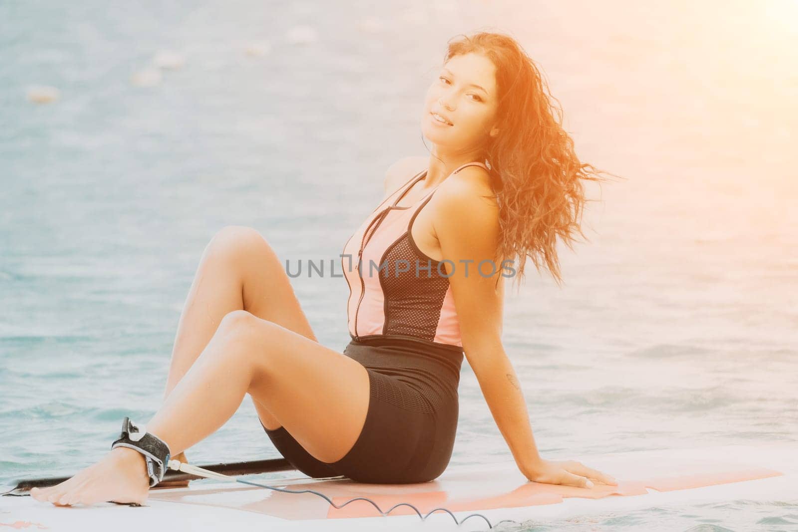 Close up shot of beautiful young caucasian woman with black hair and freckles looking at camera and smiling. Cute woman portrait in a pink bikini posing on sup board in the sea by panophotograph