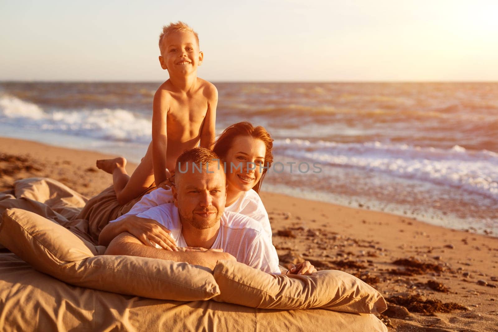 Dad tosses his son up. Lie on a bed by the sea at sunset. Family vacation on the sandy beach. Young family have fun on summer vacation.