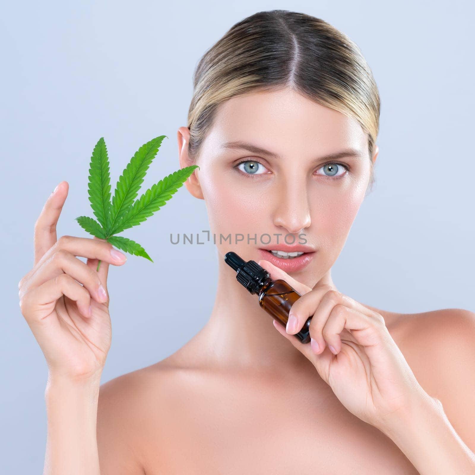 Alluring portrait of beautiful woman holding green leaf with CBD oil bottle. by biancoblue