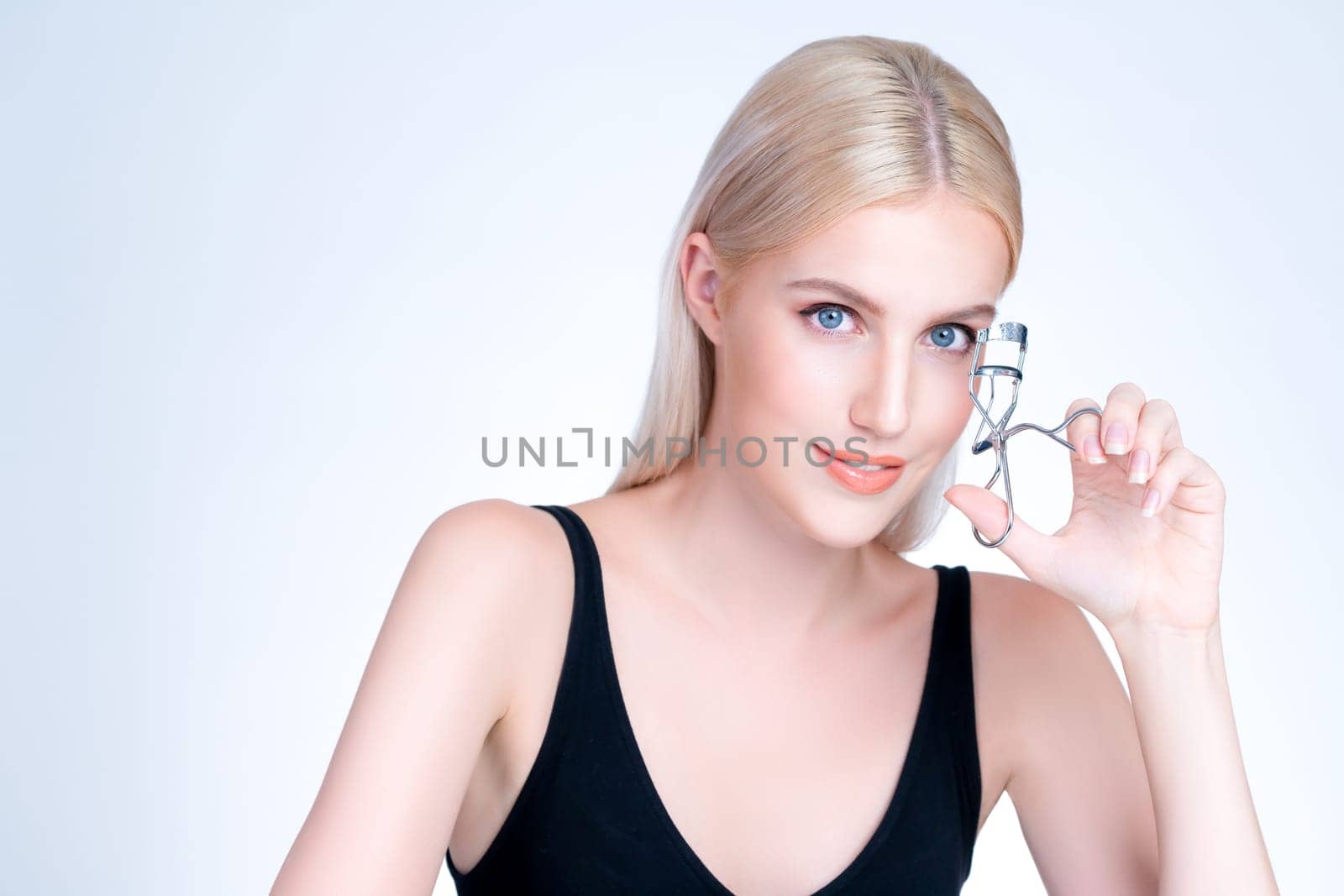 Personable woman correct eyelash curler with alluring facial makeup by biancoblue