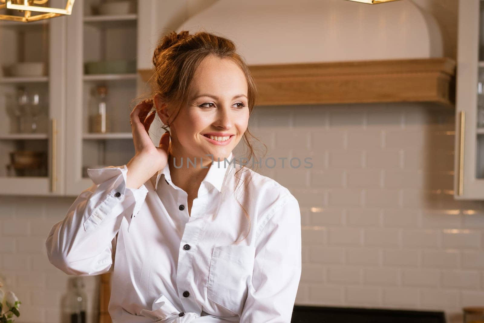 portrait of a young happy woman in a white shirt in the kitchen looking to the side