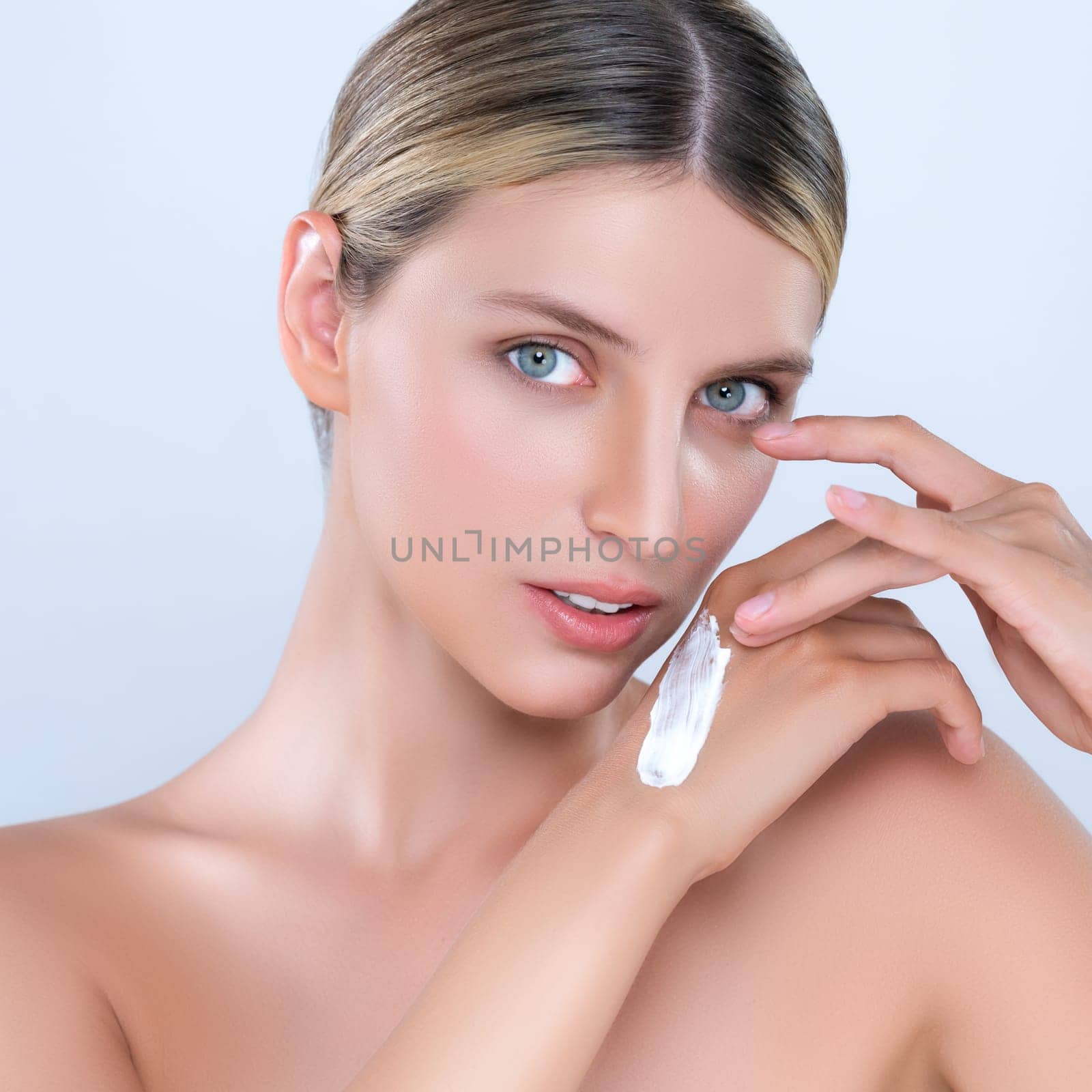 Alluring beautiful woman applying moisturizer cream on her hand for perfect skincare treatment in isolated background. Caucasian women portrait with skin rejuvenation and cosmetology concept.