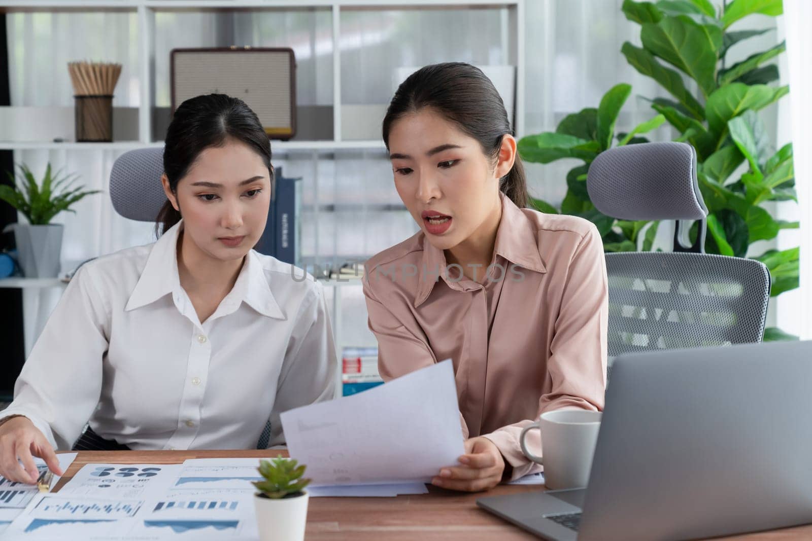 Two young office lady colleagues collaborating in modern office workspace, engaging in discussion and working together on laptop, showcasing their professionalism as modern office worker. Enthusiastic