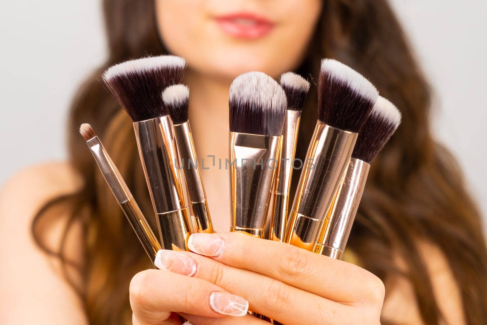 Golden makeup brushes in front of woman face.