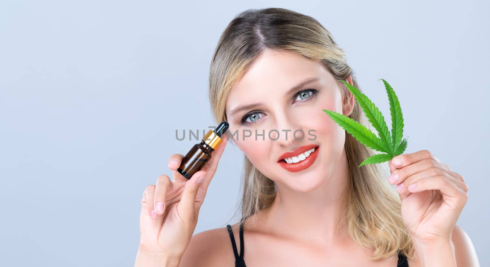 Alluring portrait of beautiful woman holding green leaf with CBD oil bottle. by biancoblue
