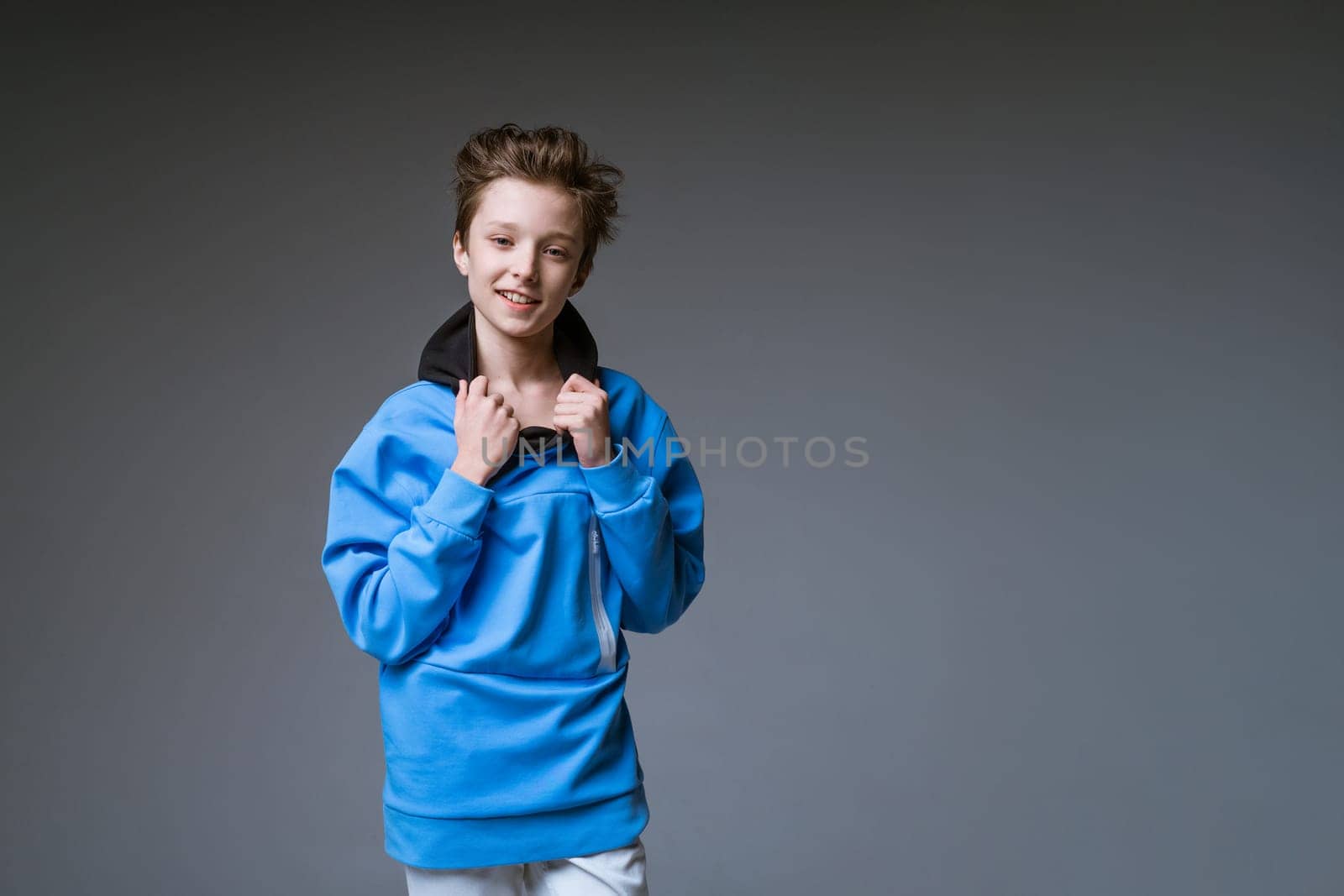 Portrait of a cute guy of European appearance with a snow-white toothy smile in a blue sweatshirt posing on a gray background