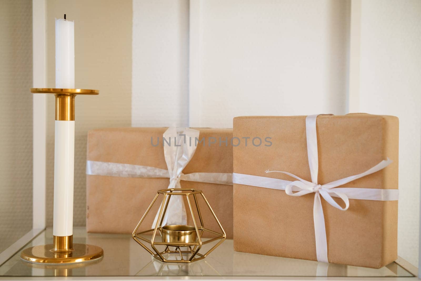 gift boxes packed with craft paper with a white bow on a shelf with a candlestick,