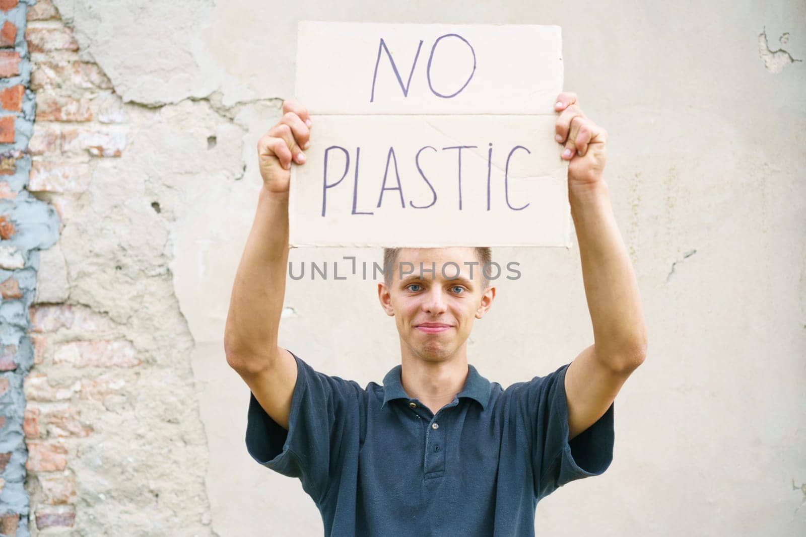 Caucasian guy holding the inscription no plastic. Environmental protection concept from garbage pollution . Young man protesting with placard banning plastic against cement wall background