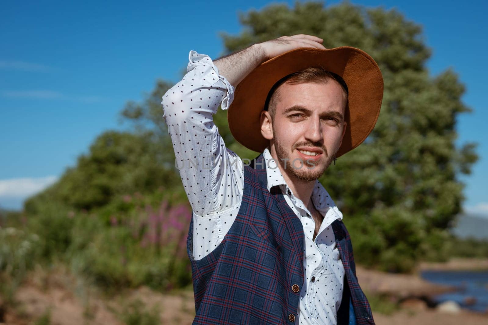Young handsome man in a shirt and a hat on nature looks to the side during the day in summer