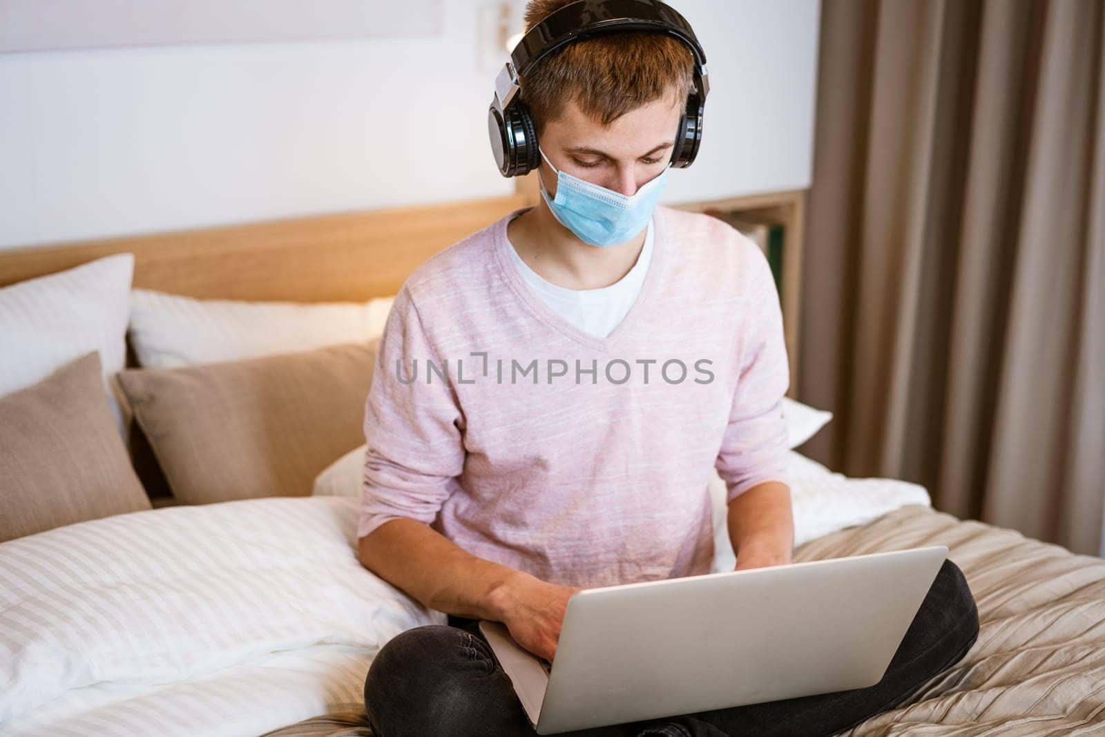 young man in headphones and protective mask at home with laptop by EkaterinaPereslavtseva