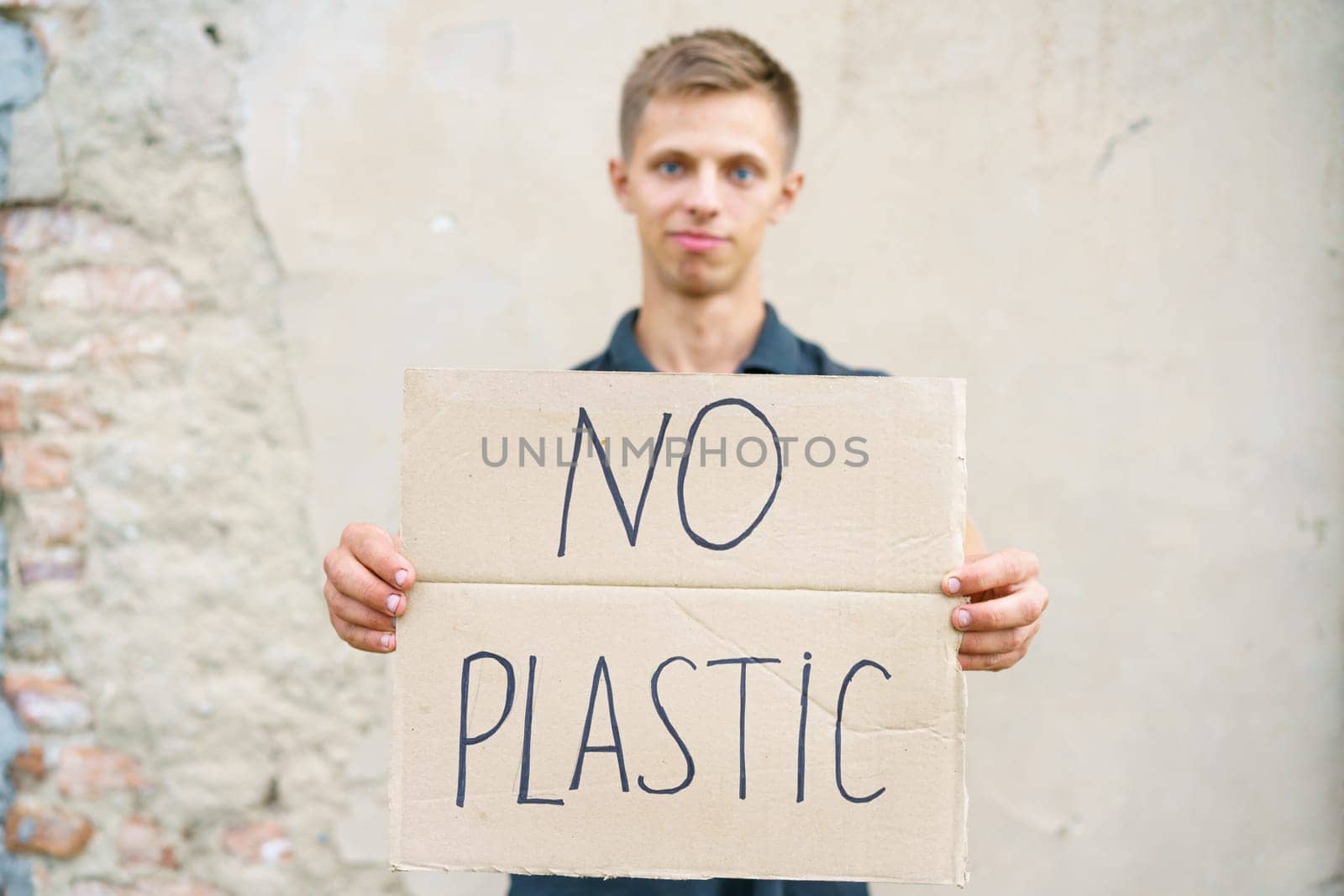 Young man with the inscription on the cardboard no plastic. Caucasian guy at a demonstration against environmental pollution, to help protect the environment. For a clean eco system on the planet