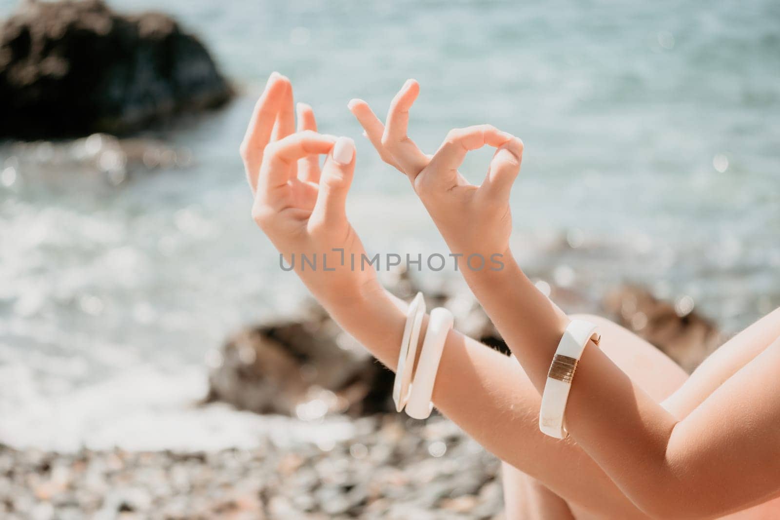 Close up Yoga Hand Gesture of Woman Doing an Outdoor meditation. Blurred sea background. Woman on yoga mat in beach meditation, mental health training or mind wellness by ocean, sea by panophotograph