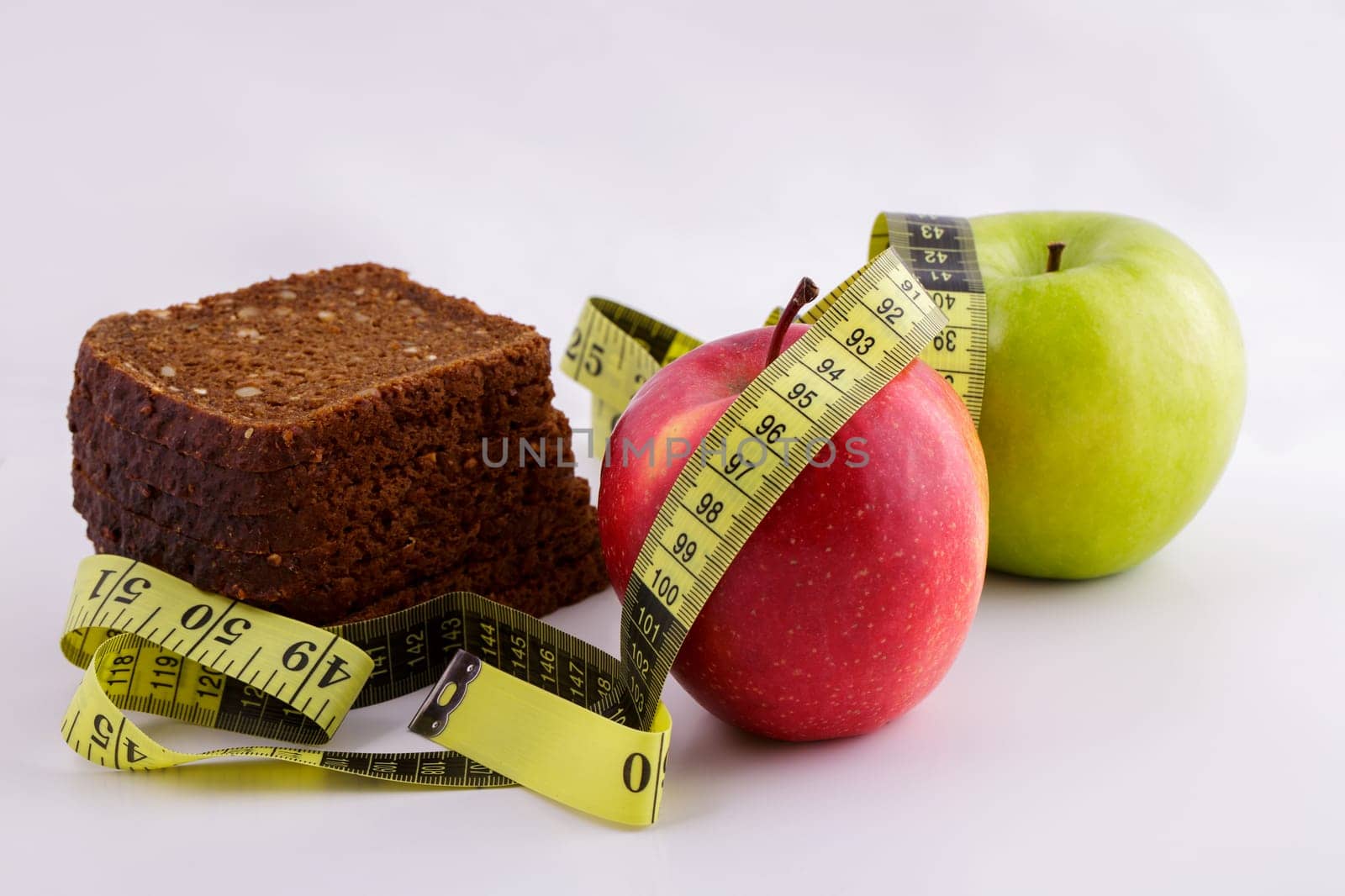 Black sliced bread and green and red apples lie on a white background with a yellow measuring tape, diet concept