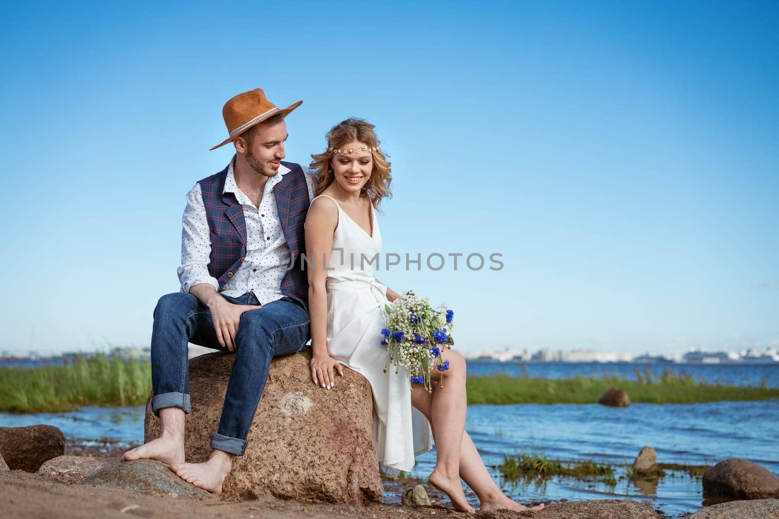 happy caucasian couple man and woman on the beach, summer day holding a bouquet of flowers in her hand