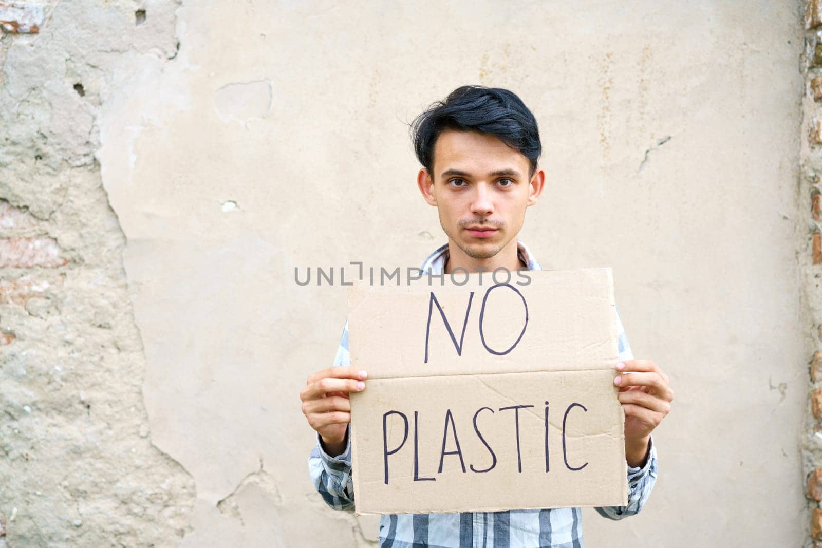 Young man with the inscription on the cardboard no plastic. Caucasian guy at a demonstration against environmental pollution, to help protect the environment. For a clean eco system on the planet