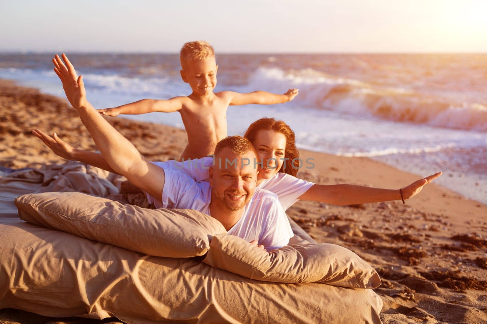 Dad tosses his son up. Lie on a bed by the sea at sunset. by EkaterinaPereslavtseva