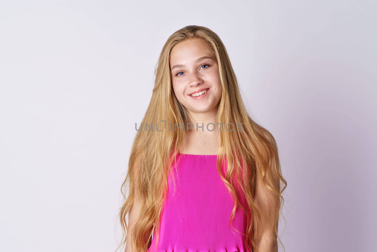 Portrait of a cute girl of blonde Caucasian ethnicity posing on a white background in pink clothes close-up. Happy teenager