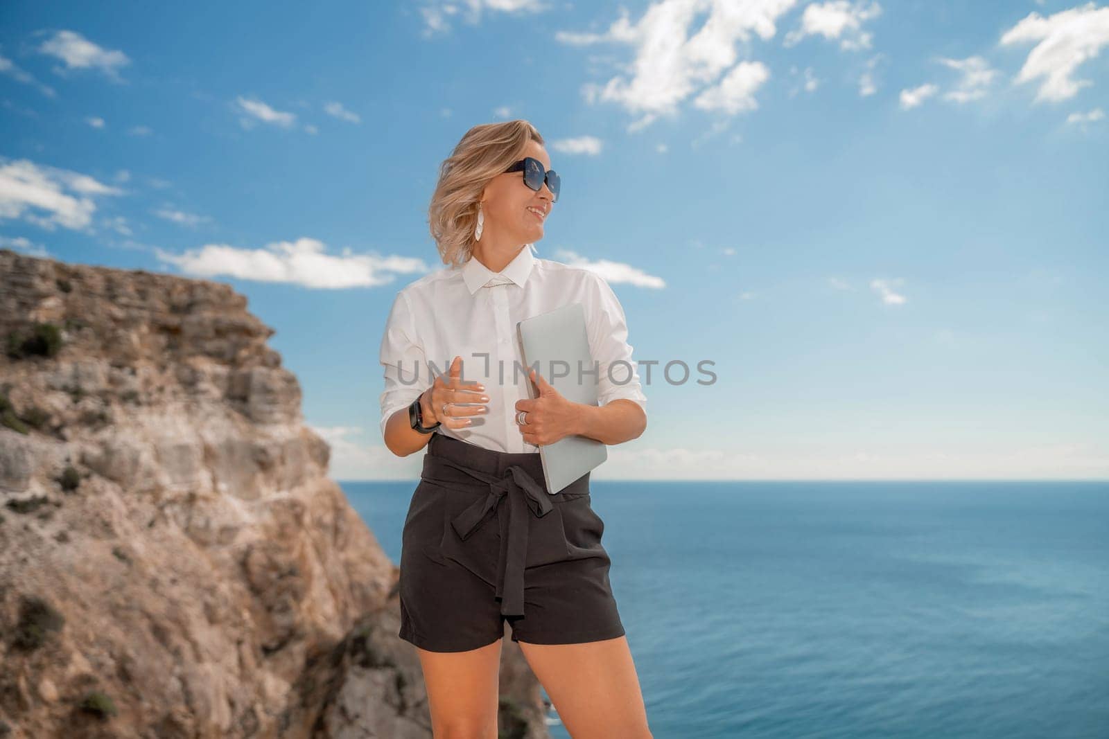 Freelance women sea working on a computer. Pretty middle aged woman with computer and phone outdoors with beautiful sea view. The concept of remote work. by Matiunina