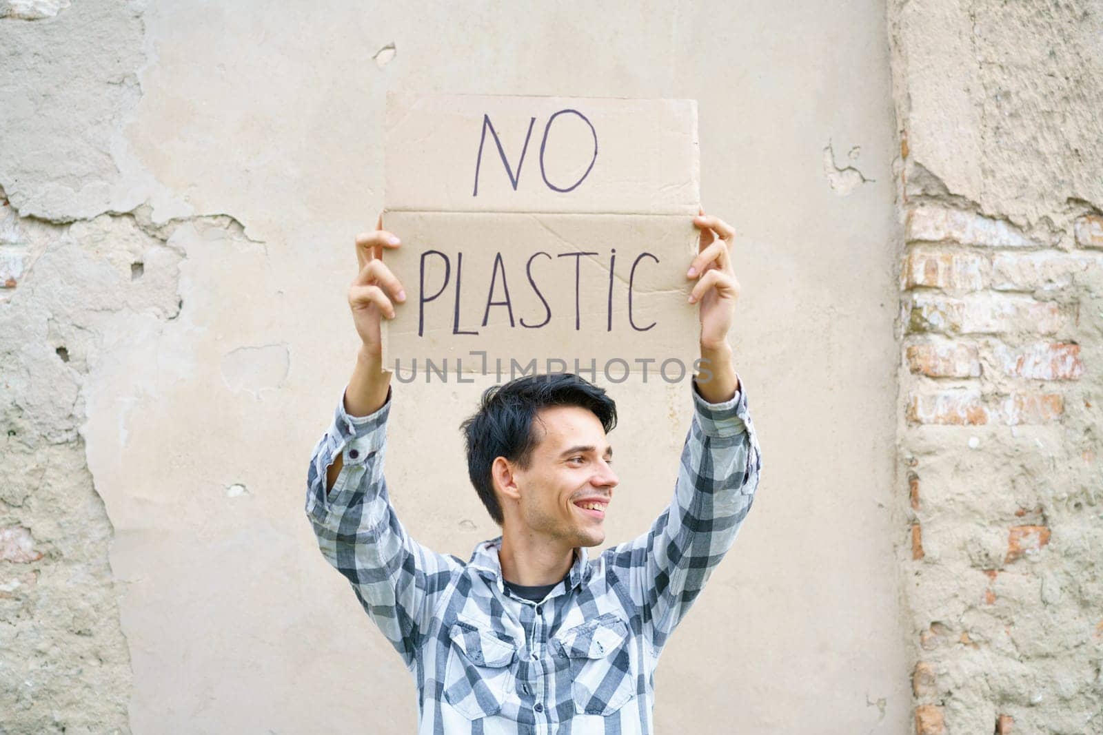 Caucasian guy holding the inscription no plastic. Environmental protection concept from garbage pollution . Young man protesting with placard banning plastic against cement wall background