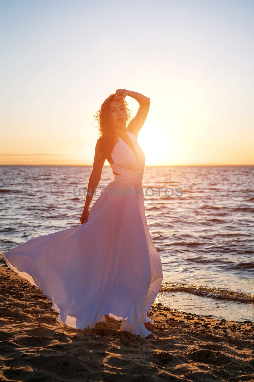 Beautiful woman posing on the beach at sunset in a white dress by EkaterinaPereslavtseva