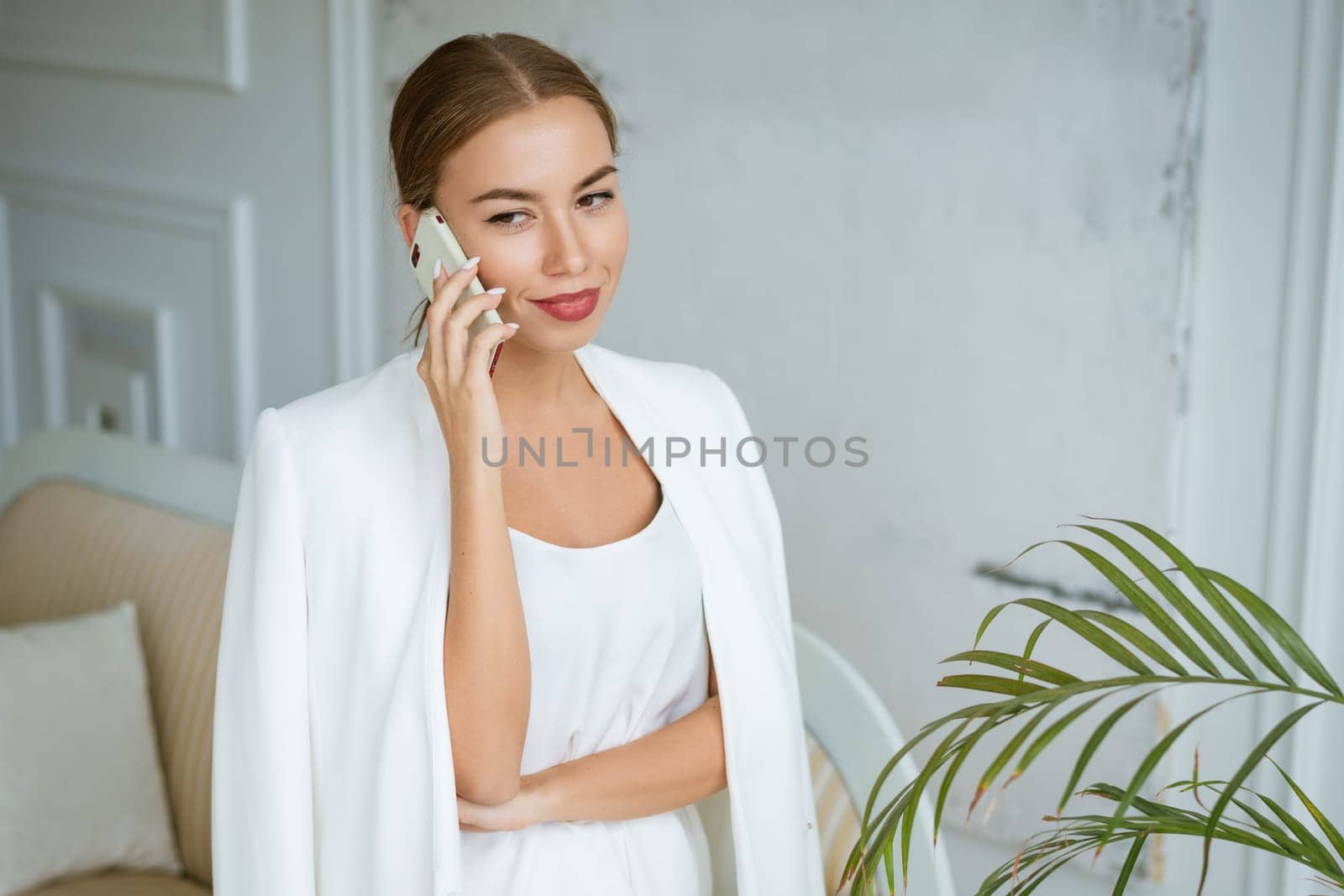 Successful young and beautiful woman of Caucasian ethnicity in a white jacket and dress talking on the phone, beautiful make-up hairstyle. Happy confident girl