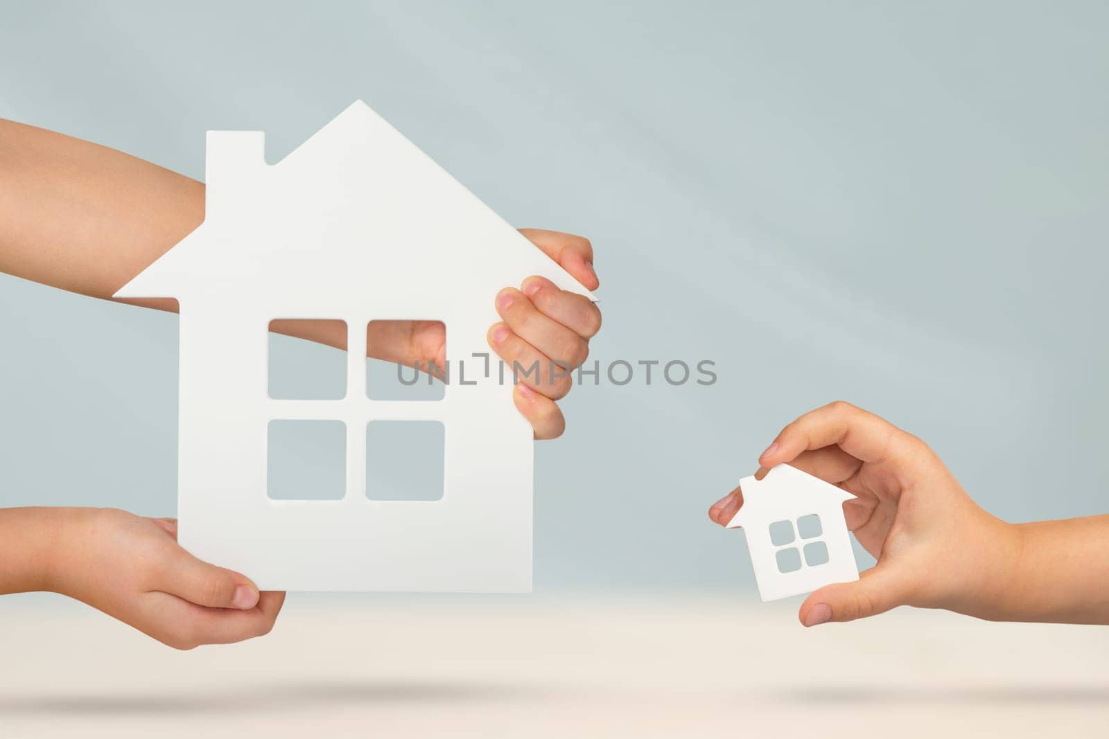 Choice between big or small house. Buying property,property comparison before buying. Model of a large and small white house in the hands on a blurred background. Buy a house or apartment, copy space