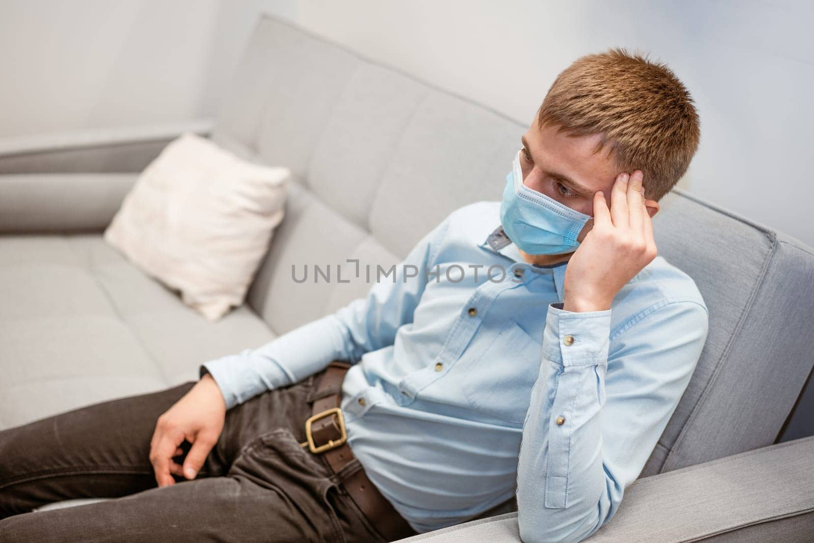 young guy sitting on the couch wearing a medical mask by EkaterinaPereslavtseva