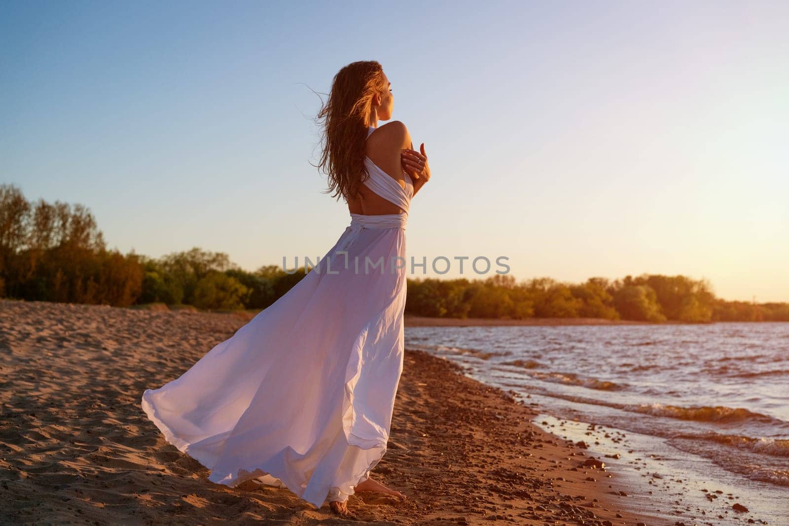 Beautiful woman posing on the beach at sunset in a white dress by EkaterinaPereslavtseva