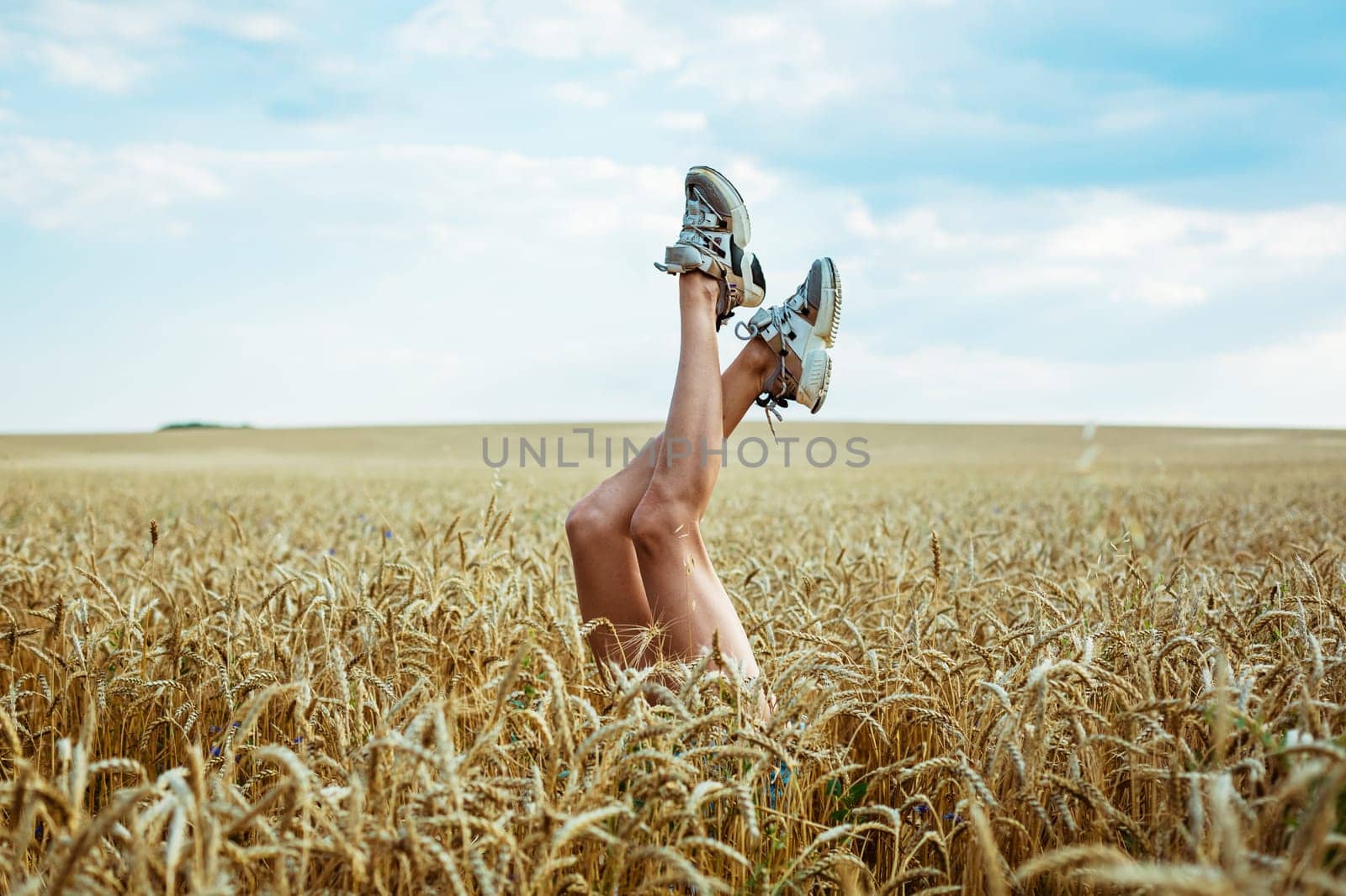 Sexy woman legs on blue sky and wheat field background. by EkaterinaPereslavtseva